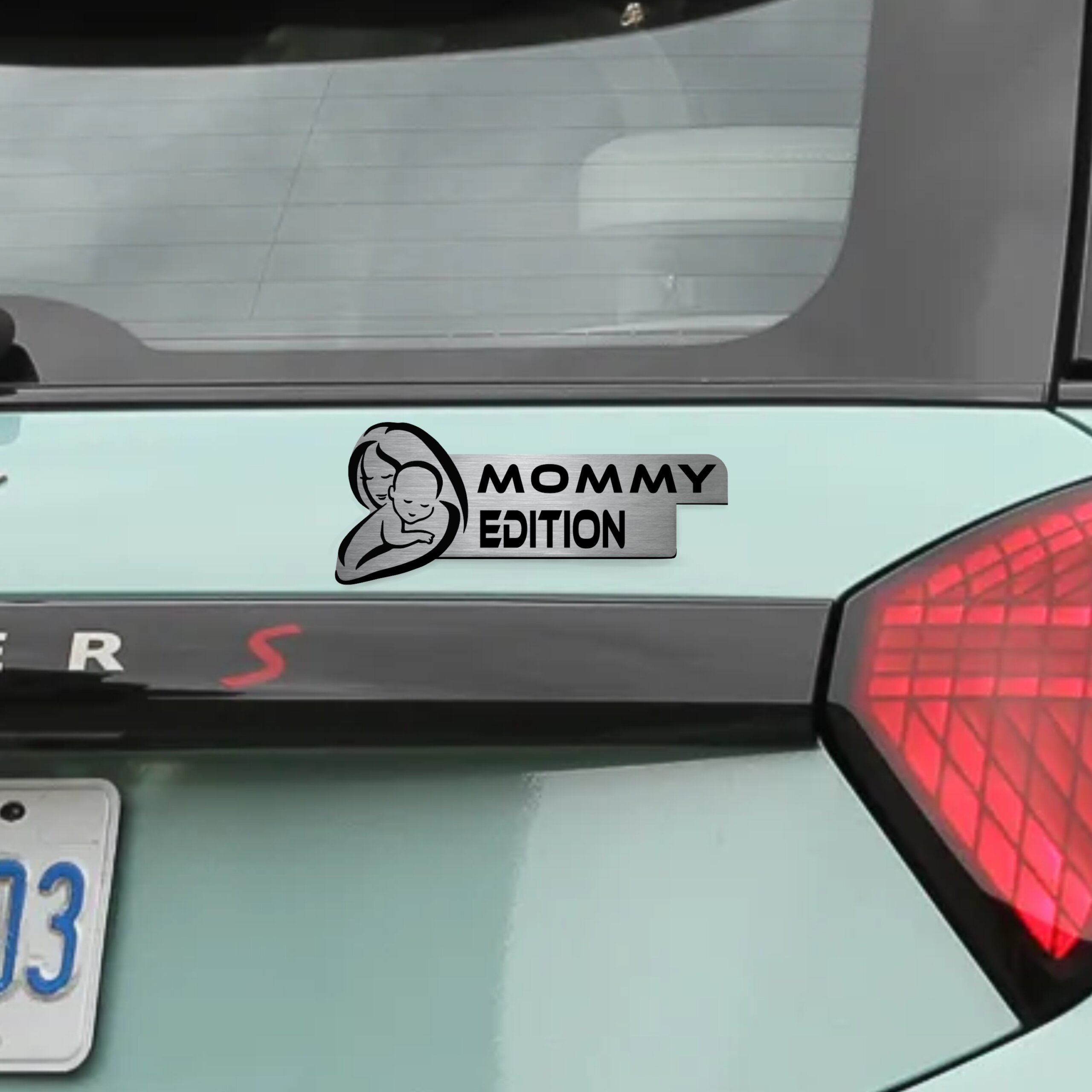 Αυτοκόλλητο Mommy Edition σε μεταλλικό φινίρισμα, με σιλουέτα μητέρας και μωρού, τοποθετημένο στο πορτ-μπαγκάζ ενός ανοιχτόχρωμου αυτοκινήτου.