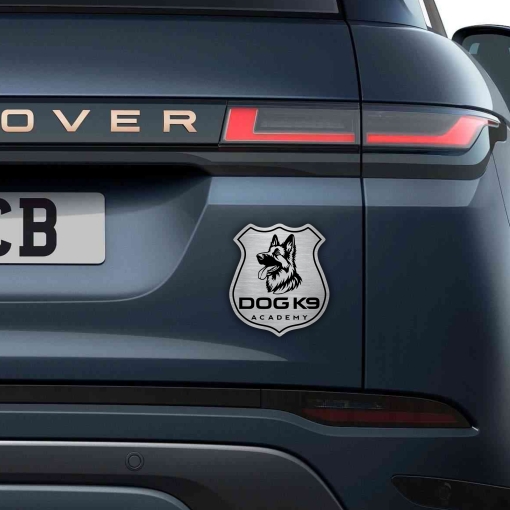 Αυτοκόλλητο Dog K9 Academy σε σχήμα αστυνομικής κονκάρδας με κεφαλή Γερμανικού Ποιμενικού, σε μεταλλικό φινίρισμα, τοποθετημένο στο πίσω μέρος ενός σκούρου SUV.
