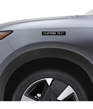 Προσωποποιημένο αυτοκόλλητο Custom Text σε μαύρο και μεταλλικό φινίρισμα, τοποθετημένο στο φτερό ενός γκρι αυτοκινήτου.