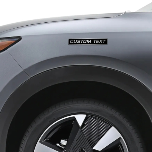 Προσωποποιημένο αυτοκόλλητο Custom Text σε μαύρο και μεταλλικό φινίρισμα, τοποθετημένο στο φτερό ενός γκρι αυτοκινήτου.