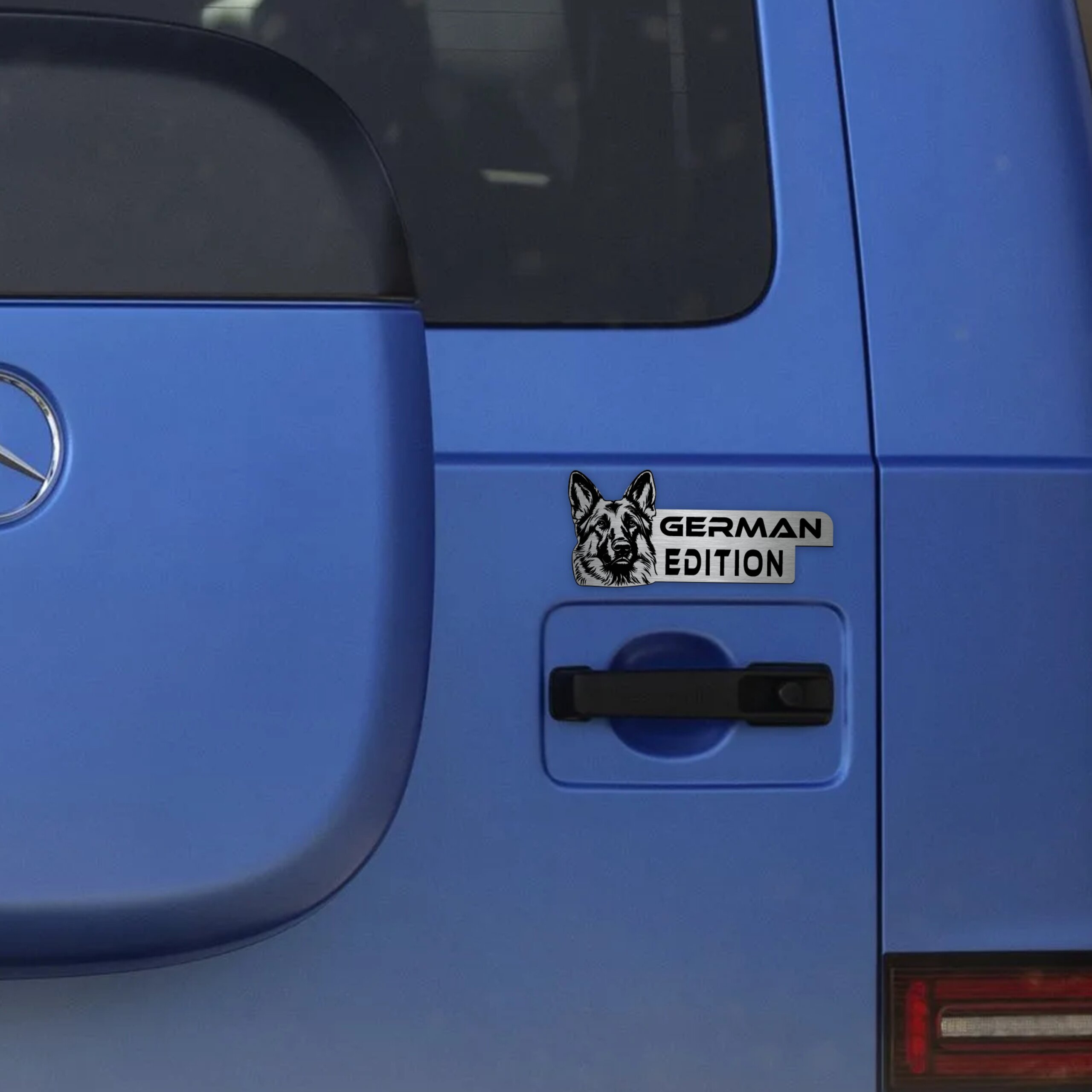 Αυτοκόλλητο German Edition σε μεταλλικό φινίρισμα, με κεφαλή Γερμανικού Ποιμενικού, τοποθετημένο στην πόρτα ενός μπλε οχήματος.