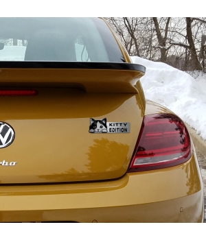 Αυτοκόλλητο Kitty Edition σε μεταλλικό φινίρισμα, με κεφαλή γάτας, τοποθετημένο στο πορτ-μπαγκάζ ενός κίτρινου αυτοκινήτου.